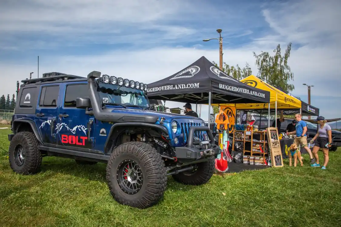 Toyo Tires Trailpass: Rugged Overland.com booth next to blue Jeep Wrangler