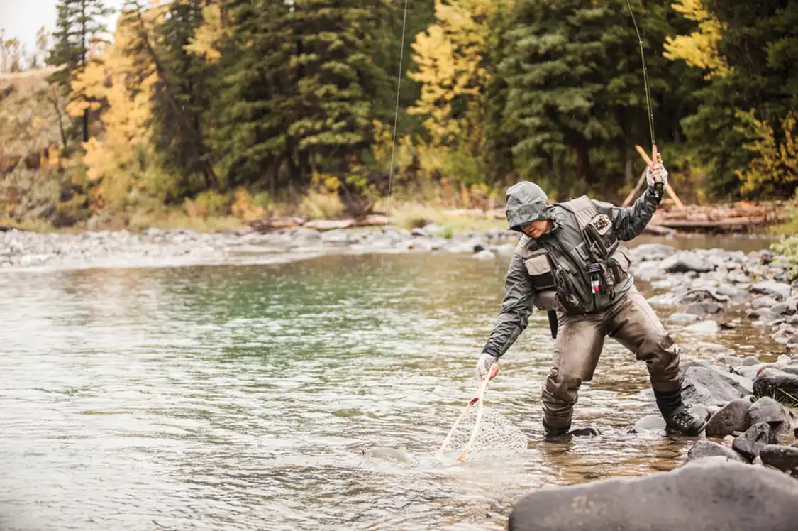 Man uses net to help catch a fish on a river.