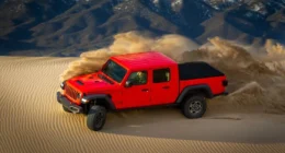 Red Jeep Gladiator turns up sand in desert.